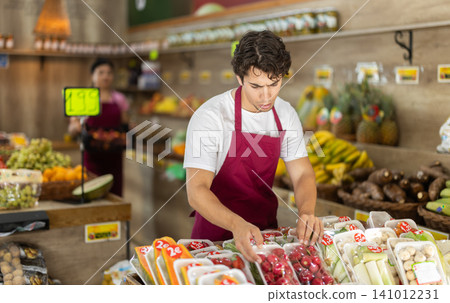 Male seller working with packaged vegetables and fruits at grocery store Male seller working with packaged vegetables and fruits at grocery store 141012231