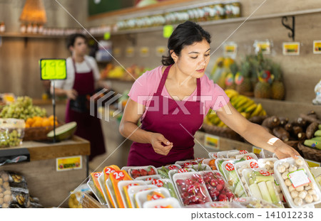 Female seller lays vegetables packed in flat transparent container. Female seller lays vegetables packed in flat transparent container. 141012238