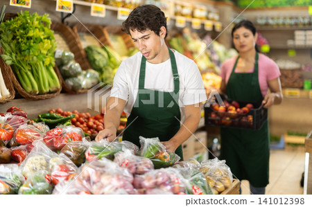 Male seller working with vegetables in plastic bags at grocery store 141012398