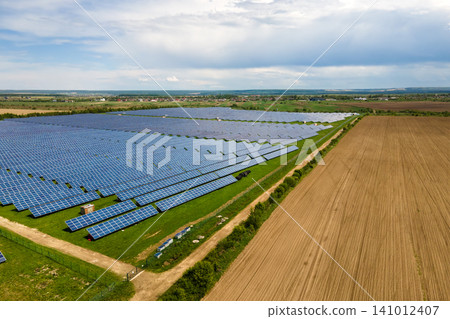 Aerial view of big sustainable electric power plant with many rows of solar photovoltaic panels for producing clean ecological electrical energy. Renewable electricity with zero emission concept. Aerial view of big sustainable electric power plant with many rows of solar photovoltaic panels for producing clean ecological electrical energy. Renewable electricity with zero emission concept. 141012407