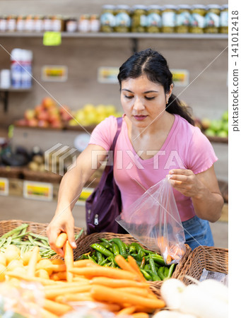 Adult woman choosing carrots in vegetable shop 141012418