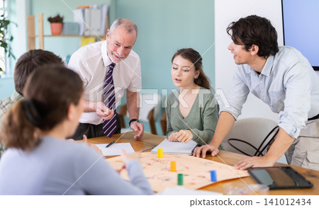 Teacher helping students play a game at the table Teacher helping students play a game at the table 141012434
