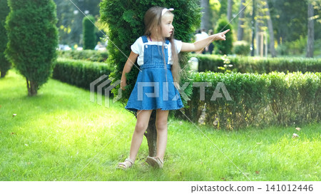 Pretty little child girl standing outdoors in green summer park pointing up with her finger. Pretty little child girl standing outdoors in green summer park pointing up with her finger. 141012446