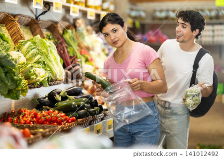 Couple shopping, examine vegetable in store and buy elect zucchini. 141012492