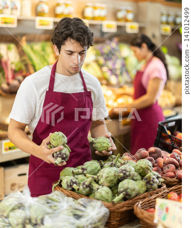 Man worker seller in grocery vegetable shop assort fruit artichoke Man worker seller in grocery vegetable shop assort fruit artichoke 141012499