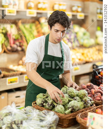 Man worker seller in grocery vegetable shop assort fruit artichoke 141012502