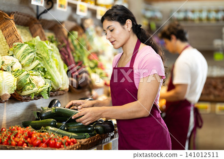 Adult woman seller puts zucchini in store 141012511
