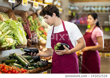 Man worker seller in grocery vegetable shop assort fruit eggplant Man worker seller in grocery vegetable shop assort fruit eggplant 141012526