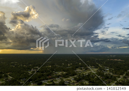 Dark stormy clouds forming on gloomy sky during heavy rainfall season over suburban town area in evening Dark stormy clouds forming on gloomy sky during heavy rainfall season over suburban town area in evening 141012549