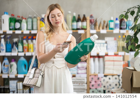 Young woman scanning QR-code on detergent in store during summer Young woman scanning QR-code on detergent in store during summer 141012554