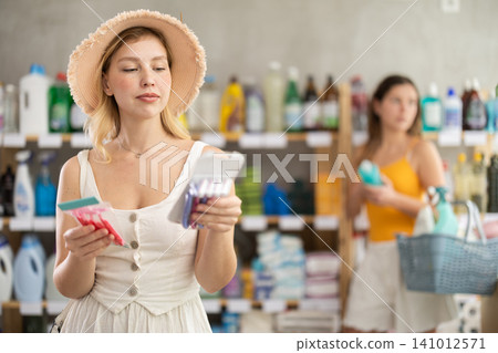 Woman consumer choose razor in household supermarket, while in background shoppers browse products Woman consumer choose razor in household supermarket, while in background shoppers browse products 141012571