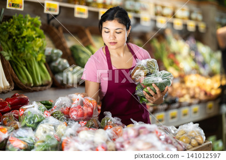 Female seller lays vegetables packed in plastic bag. Female seller lays vegetables packed in plastic bag. 141012597