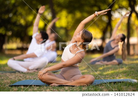 Yoga lesson visitors with girl coach perform padmasana in park Yoga lesson visitors with girl coach perform padmasana in park 141012624