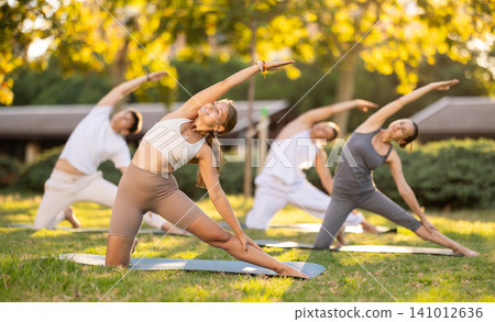 Girl enjoying group yoga session on green glade Girl enjoying group yoga session on green glade 141012636