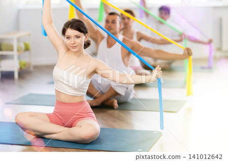 Young girl doing arm workout with band sitting cross-legged Young girl doing arm workout with band sitting cross-legged 141012642