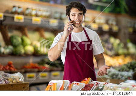 Man seller in vegetable store is talking on phone Man seller in vegetable store is talking on phone 141012644