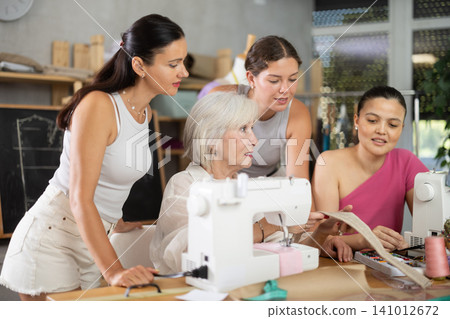 Mature female instructor demonstrating stitching at machine to younger wome Mature female instructor demonstrating stitching at machine to younger wome 141012672