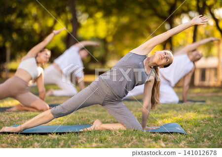 Woman performing yoga asanas during group session in park Woman performing yoga asanas during group session in park 141012678