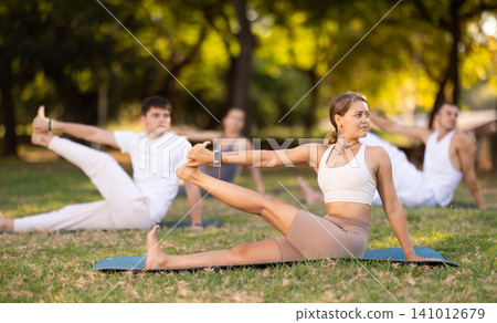 Yoga lesson visitors with coach perform eka padahastasana salamba navasana in park 141012679