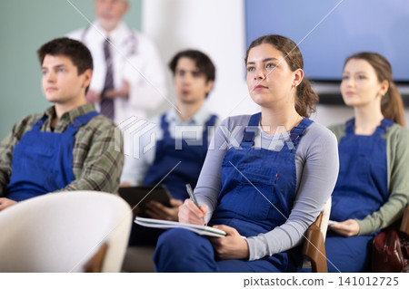 Young girl in blue overalls watching presentation with a doctor standing in background 141012725
