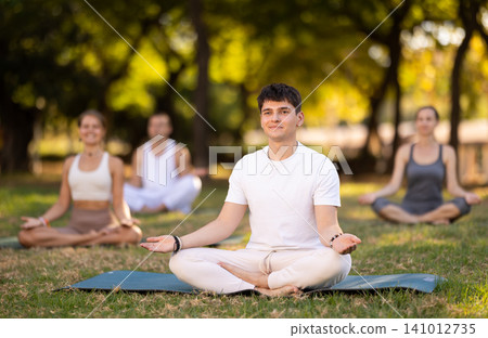 Yoga lesson visitors with guy coach perform padmasana in park Yoga lesson visitors with guy coach perform padmasana in park 141012735