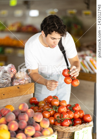 Adult man chooses tomatoes in store Adult man chooses tomatoes in store 141012748