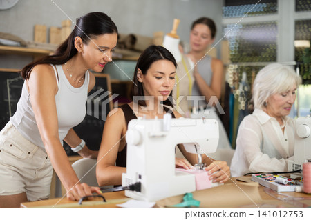 Young woman sewing with stitching-machine controlled by teacher 141012753
