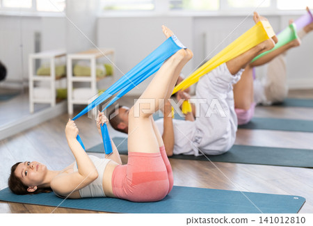 Young girl practicing leg lift with band on knees lying on the side Young girl practicing leg lift with band on knees lying on the side 141012810
