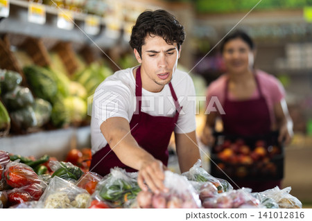Male seller working with vegetables in plastic bags at grocery store Male seller working with vegetables in plastic bags at grocery store 141012816