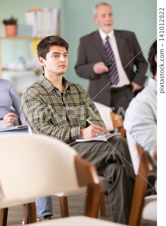 Young male student listening to lecture with teacher in background 141012822