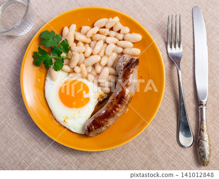 Portion of breakfast food is fried egg and pork sausage with stewed beans Portion of breakfast food is fried egg and pork sausage with stewed beans 141012848