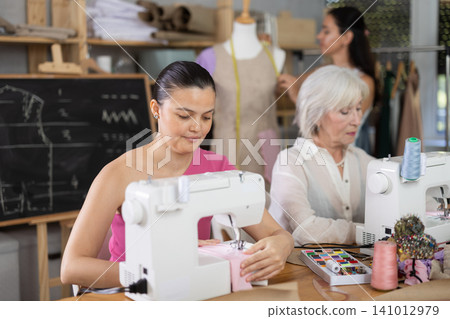 Young woman stitching at machine during group sewing course 141012979