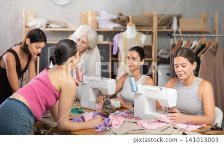 Older and younger women sewing and chatting in workroom 141013003