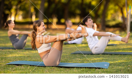 Yoga lesson visitors perform Paripurna Navasana in park Yoga lesson visitors perform Paripurna Navasana in park 141013021