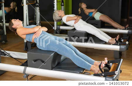 Woman in sportswear sitting on reformer platform Woman in sportswear sitting on reformer platform 141013072