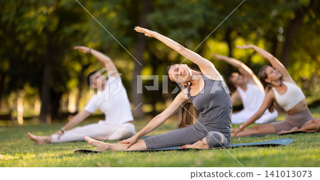 Yoga lesson visitors with coach perform Parivritta Janu Shirshasana in park Yoga lesson visitors with coach perform Parivritta Janu Shirshasana in park 141013073
