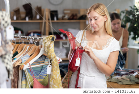 Young girl near showcase examine goods, buying handbag. Client looking for something in background Young girl near showcase examine goods, buying handbag. Client looking for something in background 141013162