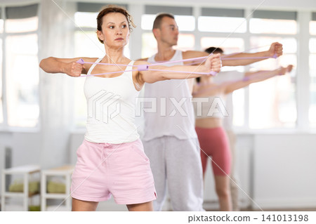Portrait of young energetic sporty woman standing and perform exercise with resistance bands in pilates studio Portrait of young energetic sporty woman standing and perform exercise with resistance bands in pilates studio 141013198