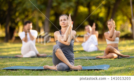 Yoga lesson visitors with coach perform Matsyendrasana in park Yoga lesson visitors with coach perform Matsyendrasana in park 141013203