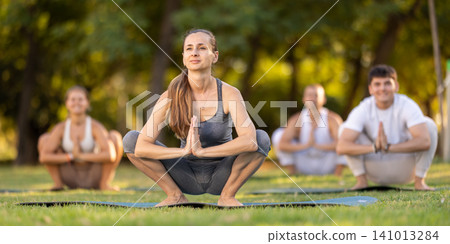 Woman performing yoga asanas during group session in park Woman performing yoga asanas during group session in park 141013284