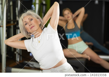 Gray-haired woman sitting on a Pilates platform 141013338