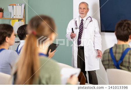 Elderly male medical professor gives lecture to group of students workers Elderly male medical professor gives lecture to group of students workers 141013396