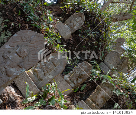 Old stone Buddhist tombstones scattered at the base of a tree 141013924