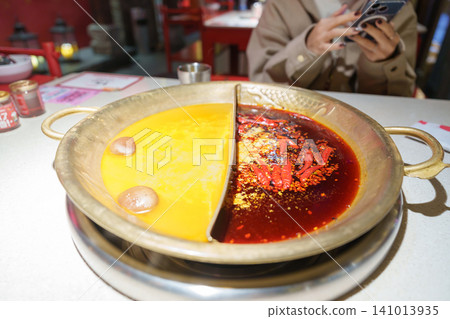 Woman tourist eating traditional hot pot or mala spicy soup in restaurant. Popular foods for tourist eating in Chengdu, Chongqing and China. Chinese Asia and Sichuan foods concept Woman tourist eating traditional hot pot or mala spicy soup in restaurant. Popular foods for tourist eating in Chengdu, Chongqing and China. Chinese Asia and Sichuan foods concept 141013935