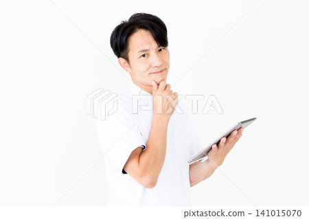 A middle-aged male acupuncturist/osteopath in a white coat, looking troubled while holding a tablet. A middle-aged male acupuncturist/osteopath in a white coat, looking troubled while holding a tablet. 141015070