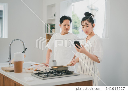 A couple cooking together in the kitchen while checking a recipe on their smartphones. A couple cooking together in the kitchen while checking a recipe on their smartphones. 141015227