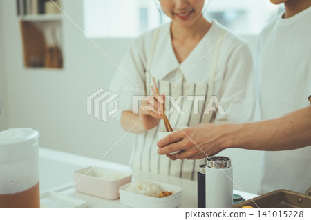 一張沒有臉孔的鏡頭,聚焦在廚房裡兩個人正在打包午餐盒配菜的手。 一張沒有臉孔的鏡頭,聚焦在廚房裡兩個人正在打包午餐盒配菜的手。 141015228