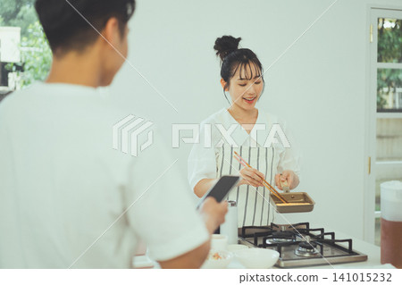 A kitchen scene showing a woman smiling and enjoying making tamagoyaki (Japanese rolled omelet). A kitchen scene showing a woman smiling and enjoying making tamagoyaki (Japanese rolled omelet). 141015232