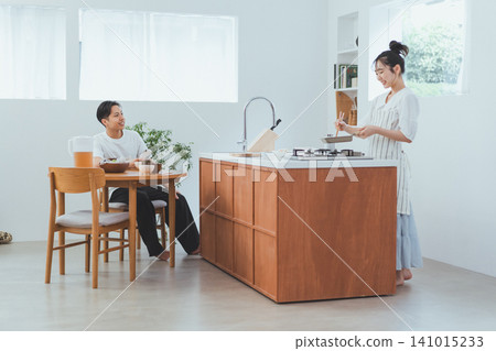 A couple's scene in a spacious living room/dining room/kitchen (LDK) where she cooks on a wooden island kitchen while her boyfriend relaxes with a smile. A couple's scene in a spacious living room/dining room/kitchen (LDK) where she cooks on a wooden island kitchen while her boyfriend relaxes with a smile. 141015233