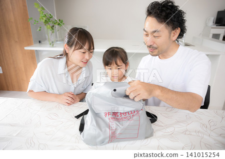 A family of three discusses disaster preparedness while checking the contents of their emergency kit, illustrating their approach to earthquake and disaster countermeasures. 141015254
